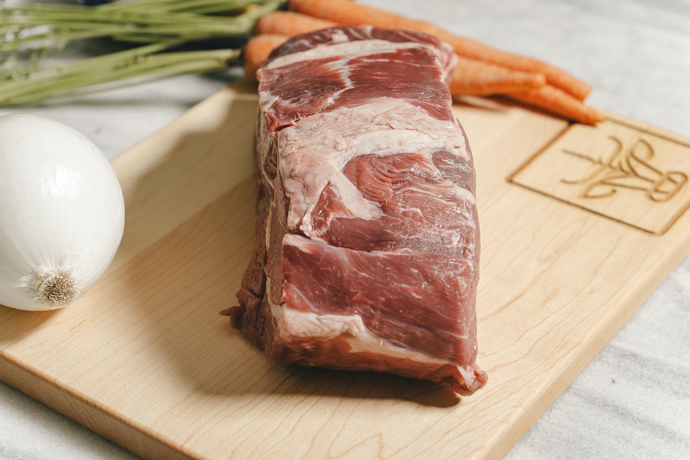 dry aged raw beef on a wooden cutting board with vegetables in the background