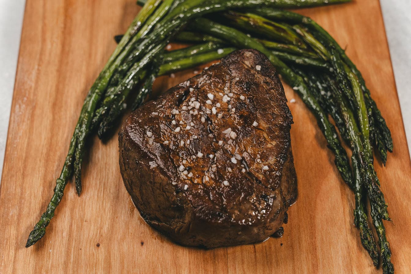 A&K steak with roasted asparagus on a wooden cutting board